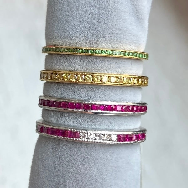 Four gemstone eternity band rings in tsavorite green garnet, yellow diamond, and ruby, all from Doyle & Doyle vintage and antique jewelry boutique
